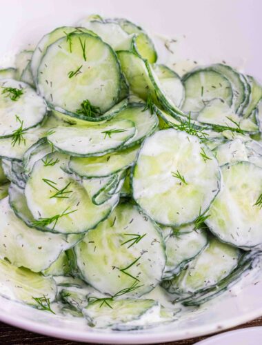 thin slices of English cucumbers in a white bowl coated with sour cream dill dressing
