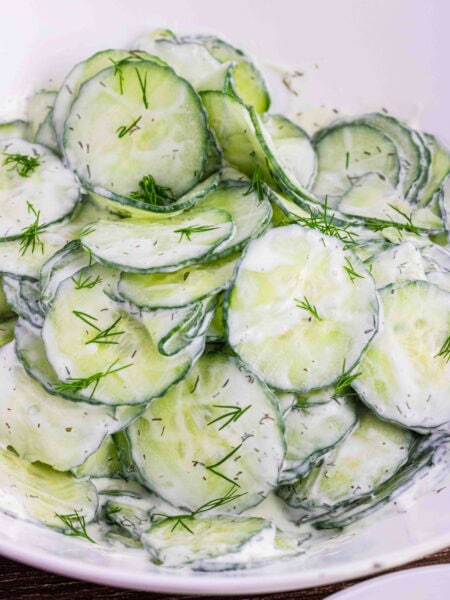 thin slices of English cucumbers in a white bowl coated with sour cream dill dressing