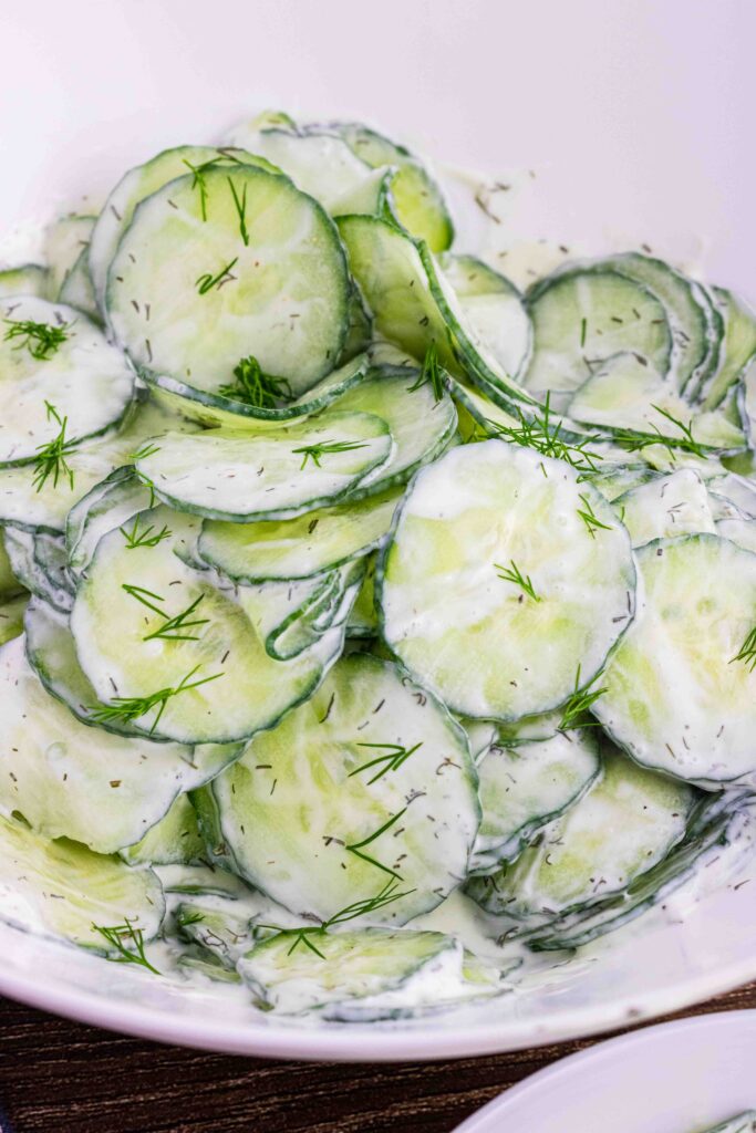 thin slices of English cucumbers in a white bowl coated with sour cream dill dressing