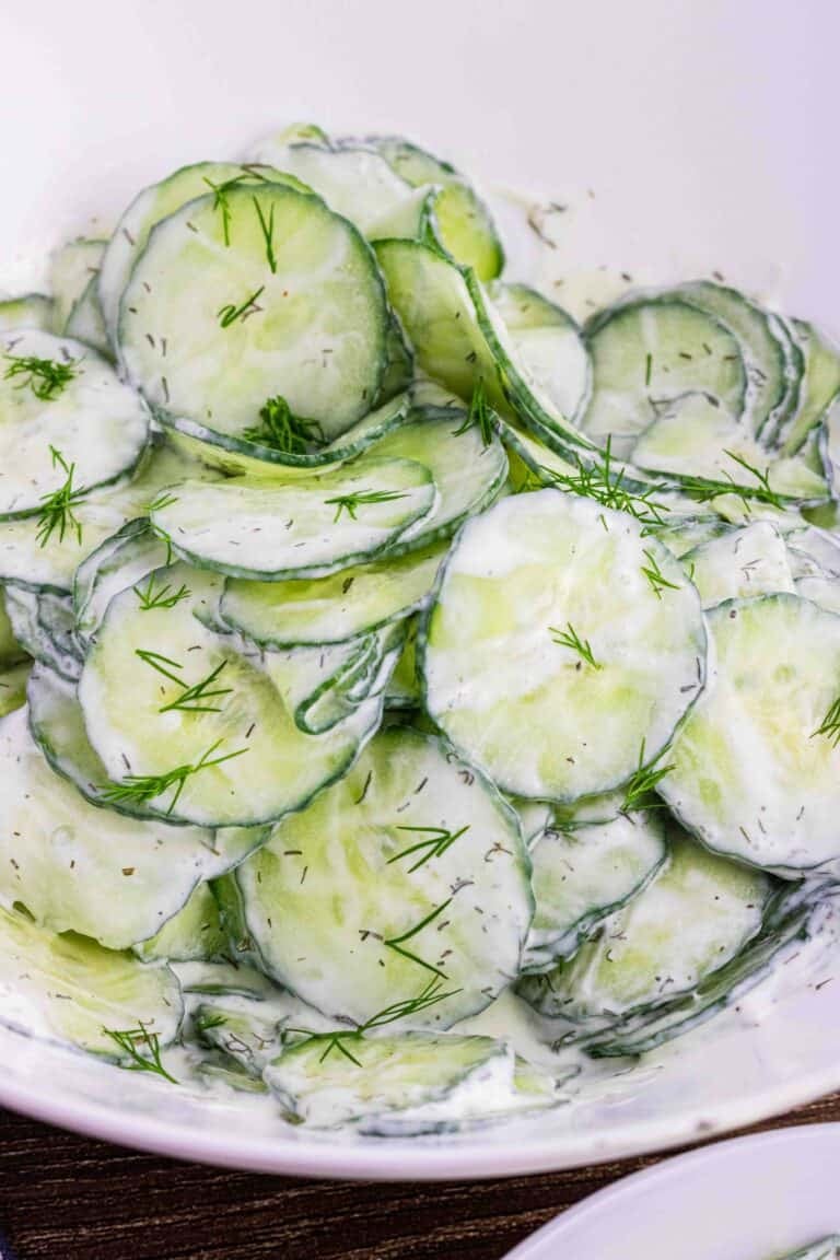 thin slices of English cucumbers in a white bowl coated with sour cream dill dressing