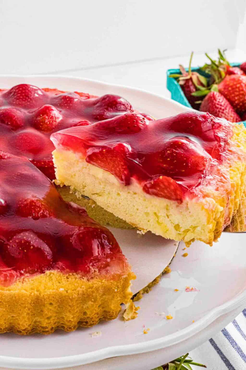 German-strawberry-sponge-cake covered with shiny red glaze. One slice is on the cake scoop and slightly elevated.
