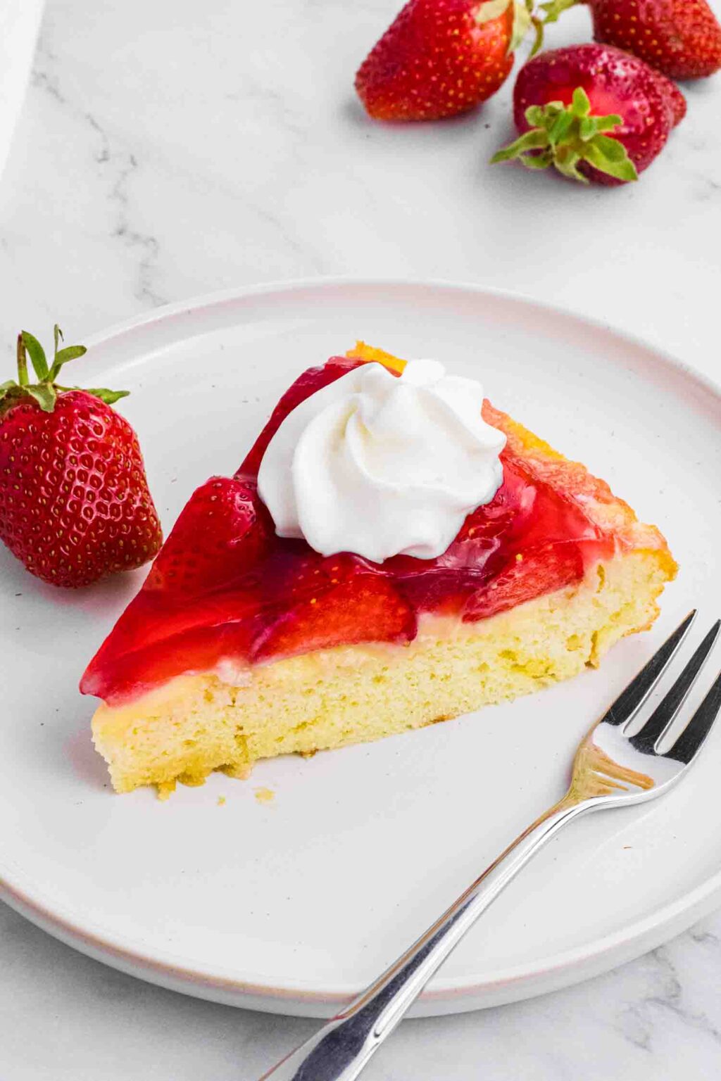 single slice of german strawberry pudding cake on a white plate with a dollop of whipping cream on the top.