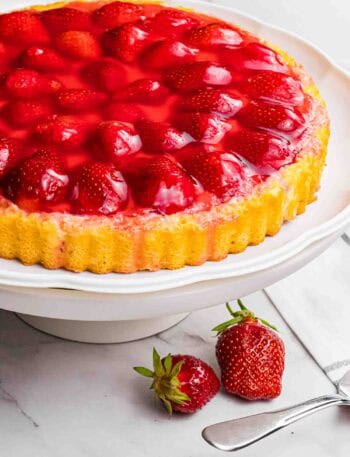strawberry sponge cake with red glazed strawberries on a white cake stand.