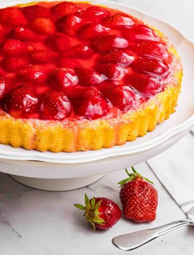 strawberry sponge cake with red glazed strawberries on a white cake stand.