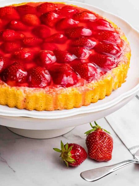 strawberry sponge cake with red glazed strawberries on a white cake stand.
