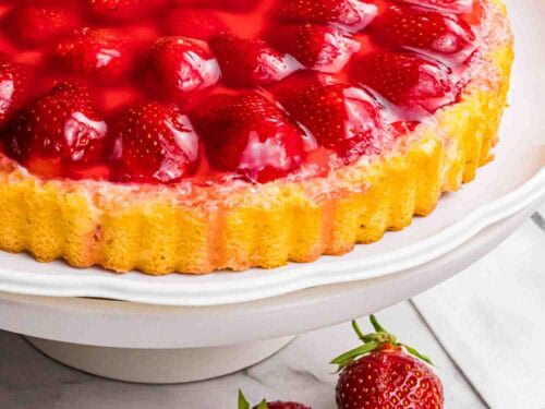 strawberry sponge cake with red glazed strawberries on a white cake stand.