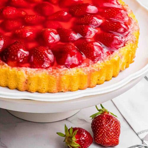 strawberry sponge cake with red glazed strawberries on a white cake stand.