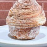 Crusty golden brown Cruffin on a white plate in front of a brick wall