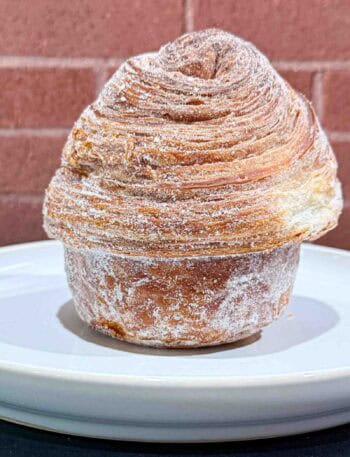 Crusty golden brown Cruffin on a white plate in front of a brick wall