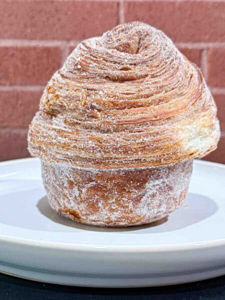 Crusty golden brown Cruffin on a white plate in front of a brick wall