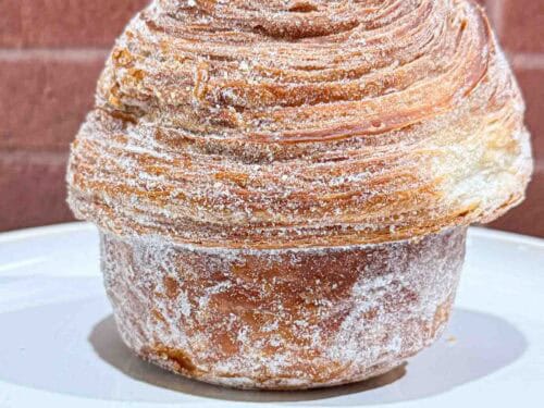 Crusty golden brown Cruffin on a white plate in front of a brick wall