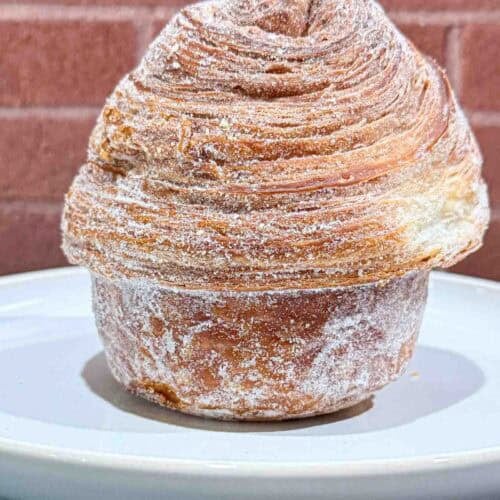 Crusty golden brown Cruffin on a white plate in front of a brick wall