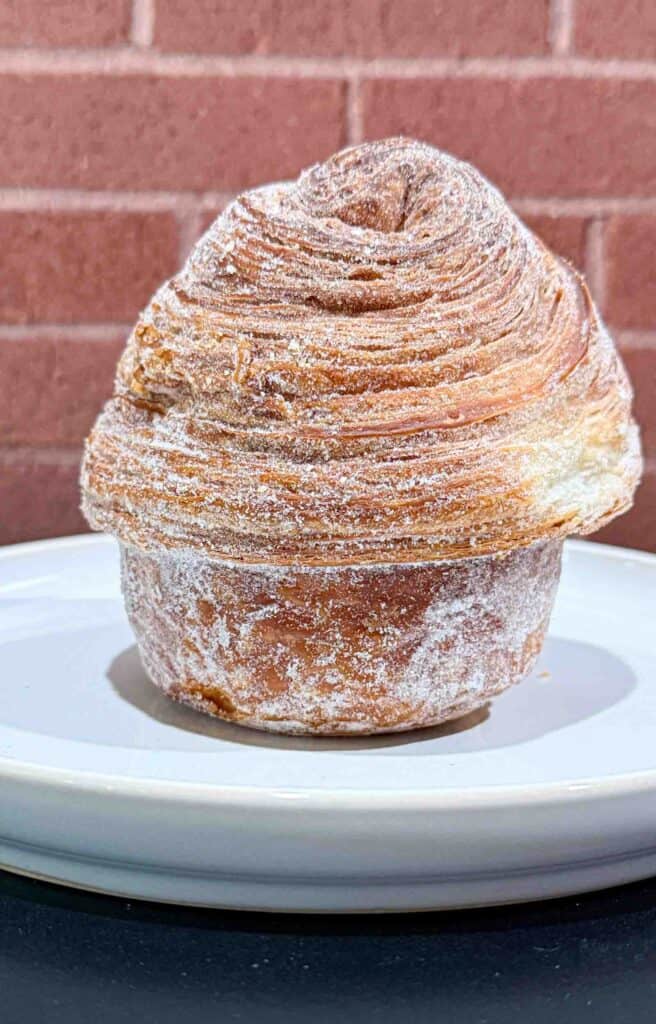 Crusty golden brown Cruffin on a white plate in front of a brick wall