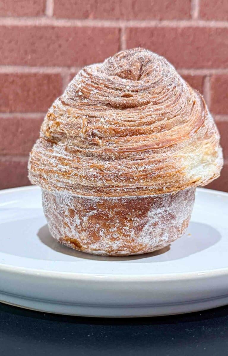 Crusty golden brown Cruffin on a white plate in front of a brick wall