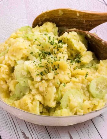 German Potato Salad in a glass bowl with two wooden salad spoons on the side
