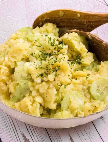 German Potato Salad in a glass bowl with two wooden salad spoons on the side