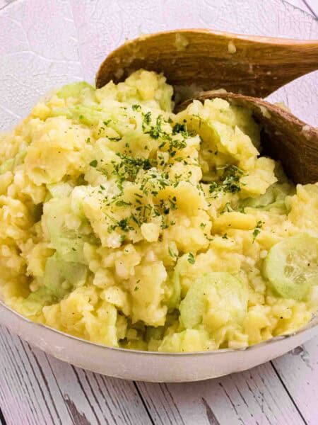 German Potato Salad in a glass bowl with two wooden salad spoons on the side