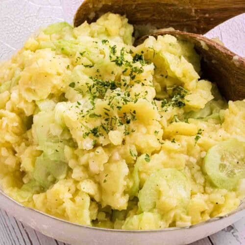 German Potato Salad in a glass bowl with two wooden salad spoons on the side