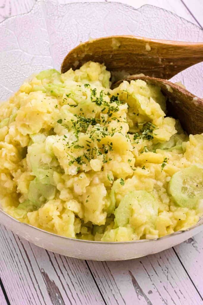 German Potato Salad in a glass bowl with two wooden salad spoons on the side