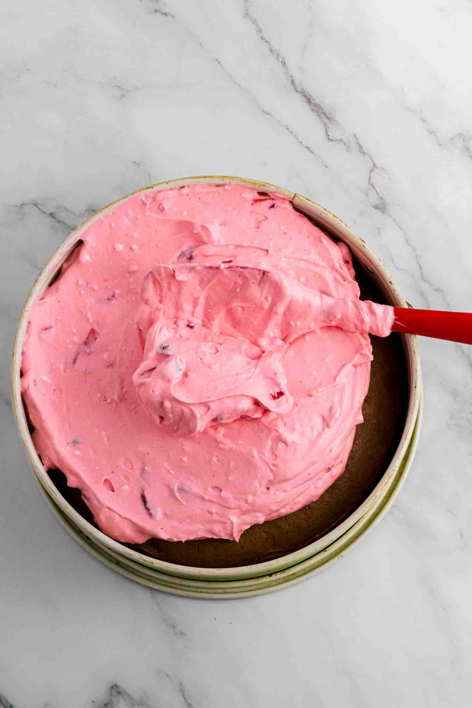 strawberry mousse being spread on the chocolate sponge for strawberry mousse cake