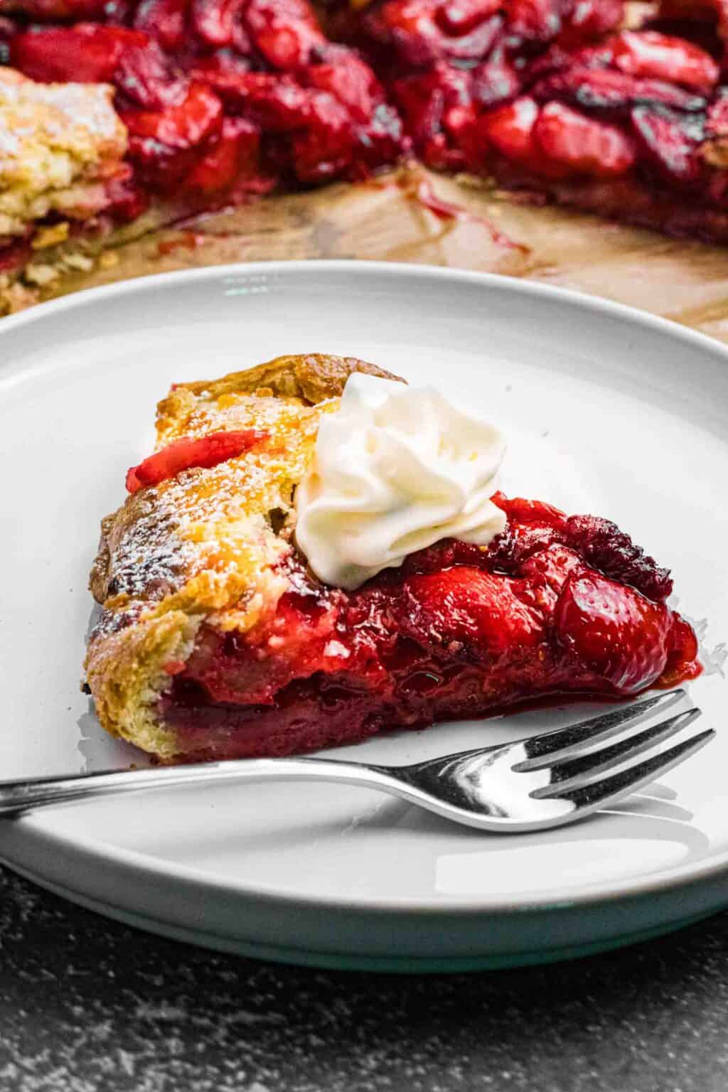 one piece of strawberry galette on a white plate topped with whipping cream