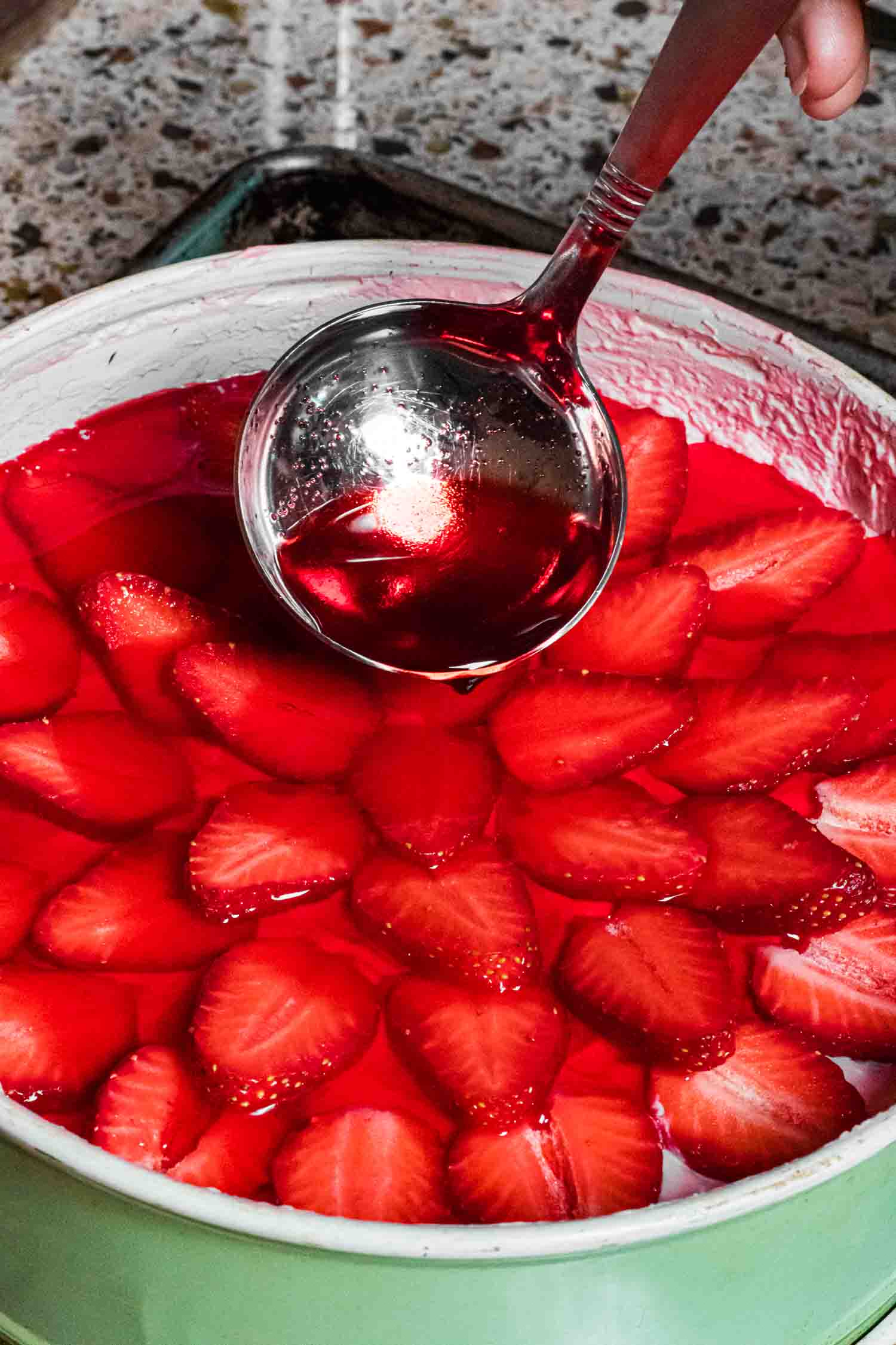 glaze is being spooned on the strawberry mousse cake