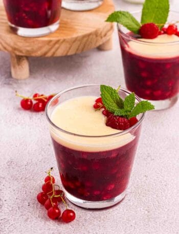 Rote Grütze or Red Berry Pudding in a Glass decorated with currants and raspberries and a layer of vanilla sauce
