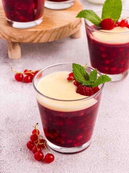 Rote Grütze or Red Berry Pudding in a Glass decorated with currants and raspberries and a layer of vanilla sauce