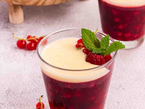 Rote Grütze or Red Berry Pudding in a Glass decorated with currants and raspberries and a layer of vanilla sauce
