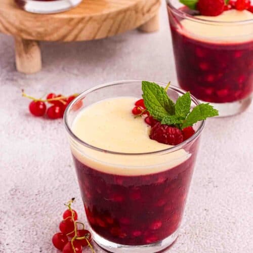 Rote Grütze or Red Berry Pudding in a Glass decorated with currants and raspberries and a layer of vanilla sauce