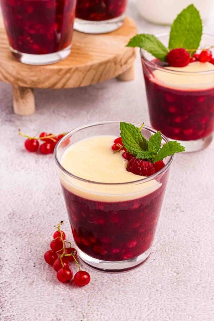 Rote Grütze or Red Berry Pudding in a Glass decorated with currants and raspberries and a layer of vanilla sauce