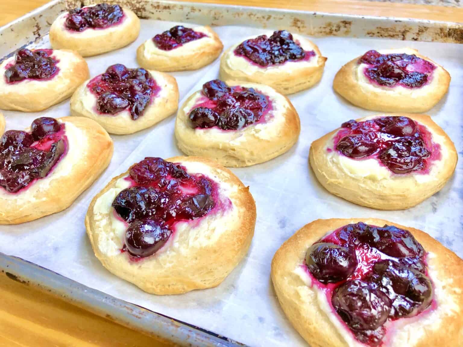 cherry danish on a backing sheet topped with cherry pie filling