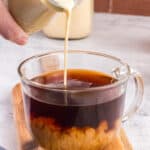 Pouring coffee creamer in a glass cup full of good coffee