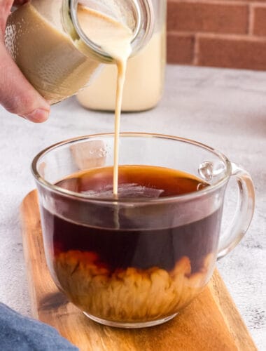Pouring coffee creamer in a glass cup full of good coffee