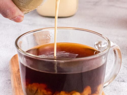 Pouring coffee creamer in a glass cup full of good coffee