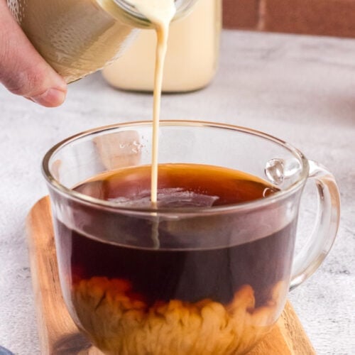 Pouring coffee creamer in a glass cup full of good coffee