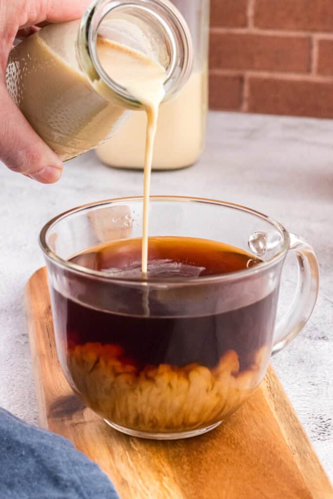Pouring coffee creamer in a glass cup full of good coffee
