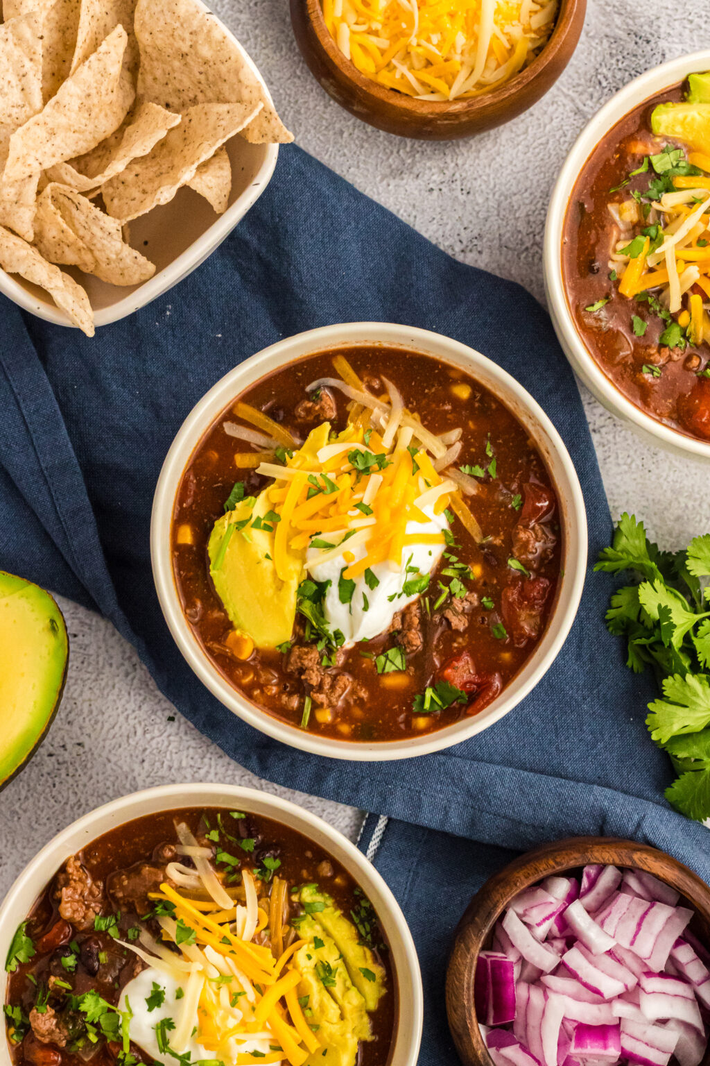 An arrangement of bowls of chili with tortilla chips and red onions on the side