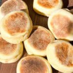 Fresh English Muffins spread out on a wooden board.