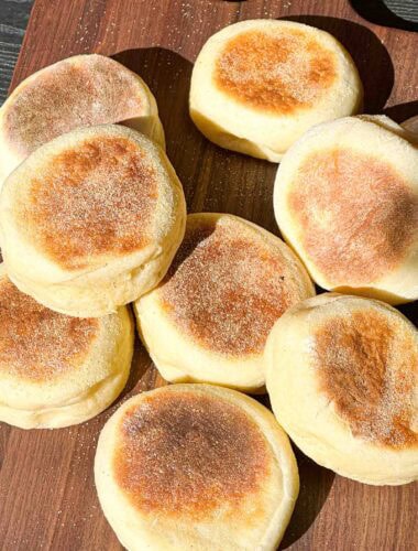 Fresh English Muffins spread out on a wooden board.