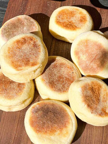 Fresh English Muffins spread out on a wooden board.