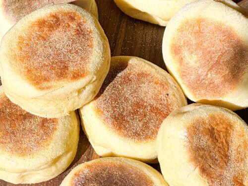 Fresh English Muffins spread out on a wooden board.