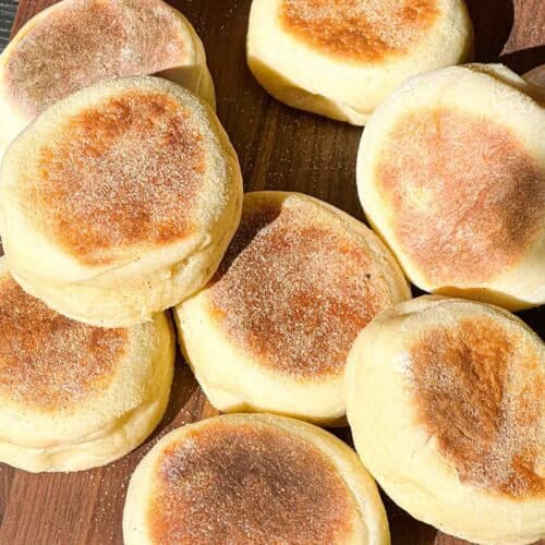 Fresh English Muffins spread out on a wooden board.