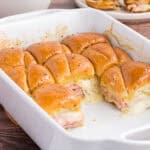 Baked Ham and Cheese Sliders in a white casserole dish. 8 leftover pieces are on the back of the casserole.