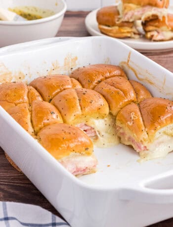 Baked Ham and Cheese Sliders in a white casserole dish. 8 leftover pieces are on the back of the casserole.