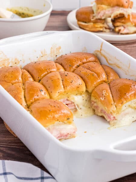Baked Ham and Cheese Sliders in a white casserole dish. 8 leftover pieces are on the back of the casserole.