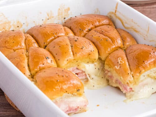 Baked Ham and Cheese Sliders in a white casserole dish. 8 leftover pieces are on the back of the casserole.