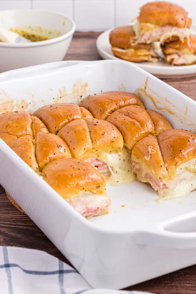 Baked Ham and Cheese Sliders in a white casserole dish. 8 leftover pieces are on the back of the casserole.