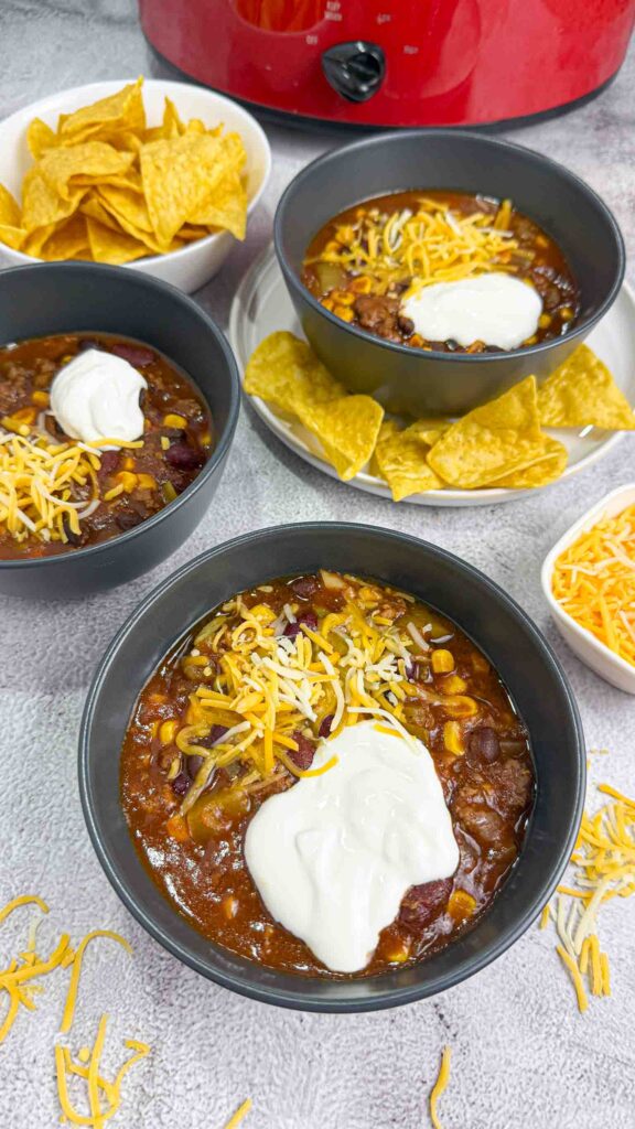 3 black bowls filled with chili and  topped with shredded cheese and sour cream