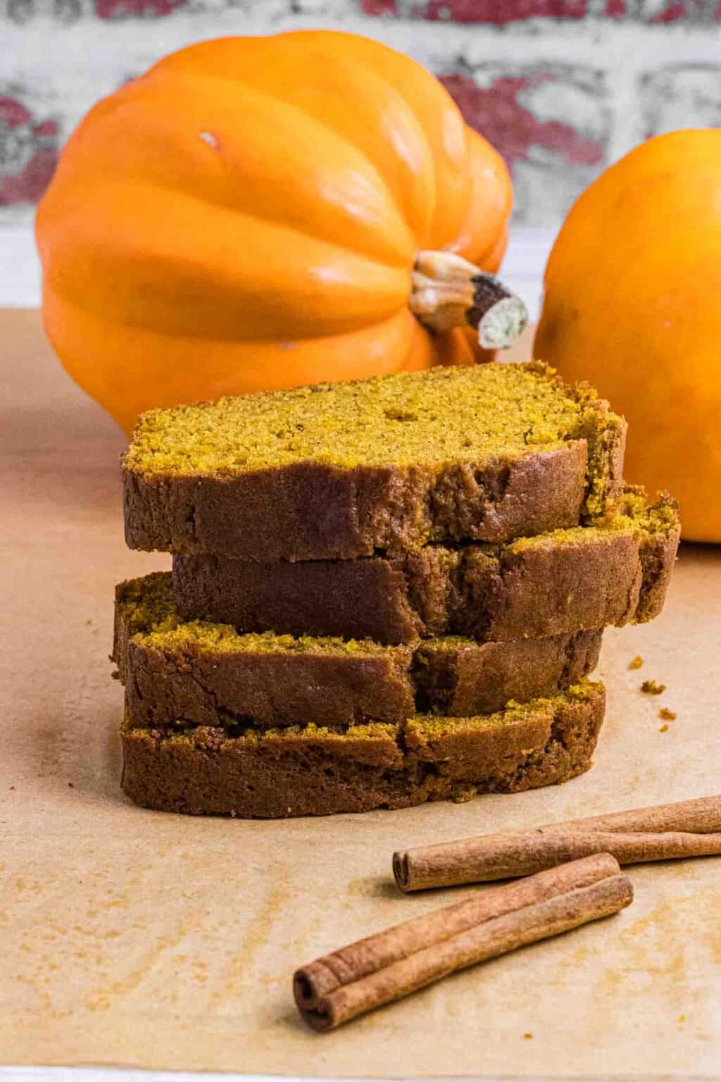 Pumpkin Bread Slices in a stack surrounded with cinnamon sticks and pumpkins